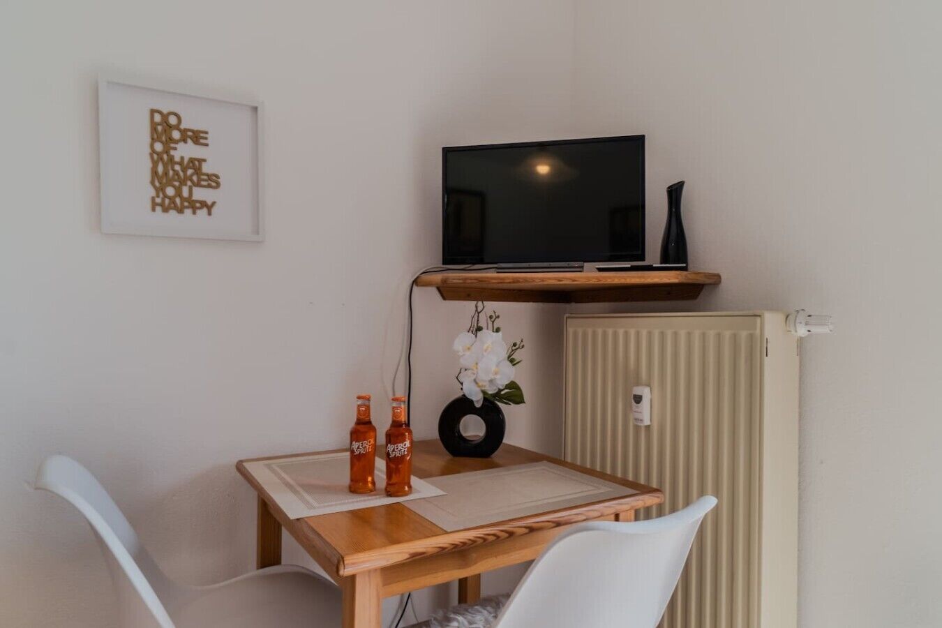 Ein kleiner Essbereich mit einem Holztisch, zwei Stühlen, einem Fernseher auf einem Regal und einer Heizung.