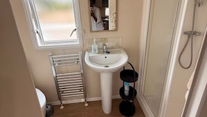 Een kleine badkamer met een wastafel, spiegel, douche en een raam.