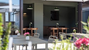 An outdoor dining area with tables and chairs, a kitchen in the background, and hanging pendant lights.
