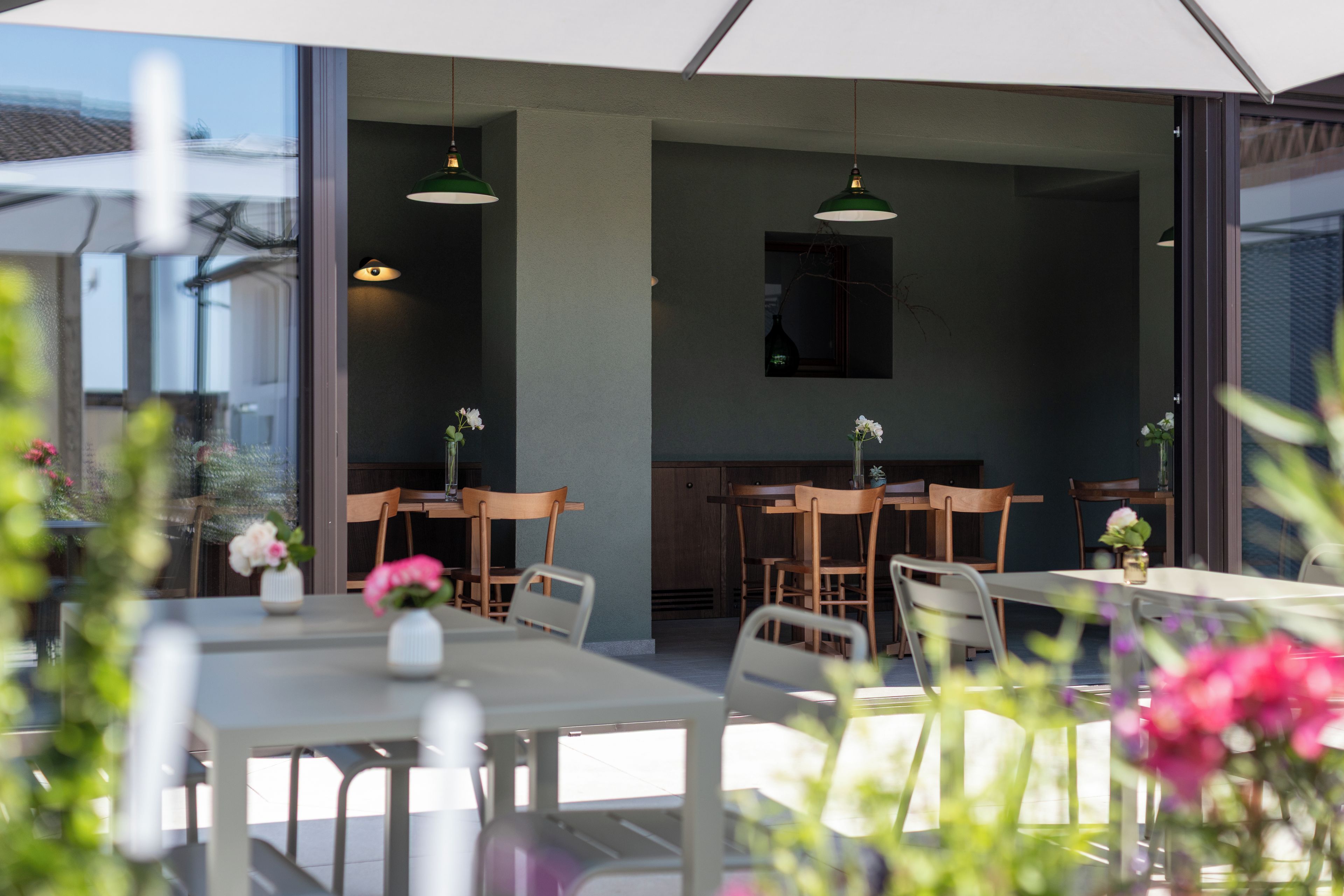 An outdoor dining area with tables and chairs, a kitchen area with wooden cabinets, and hanging pendant lights.