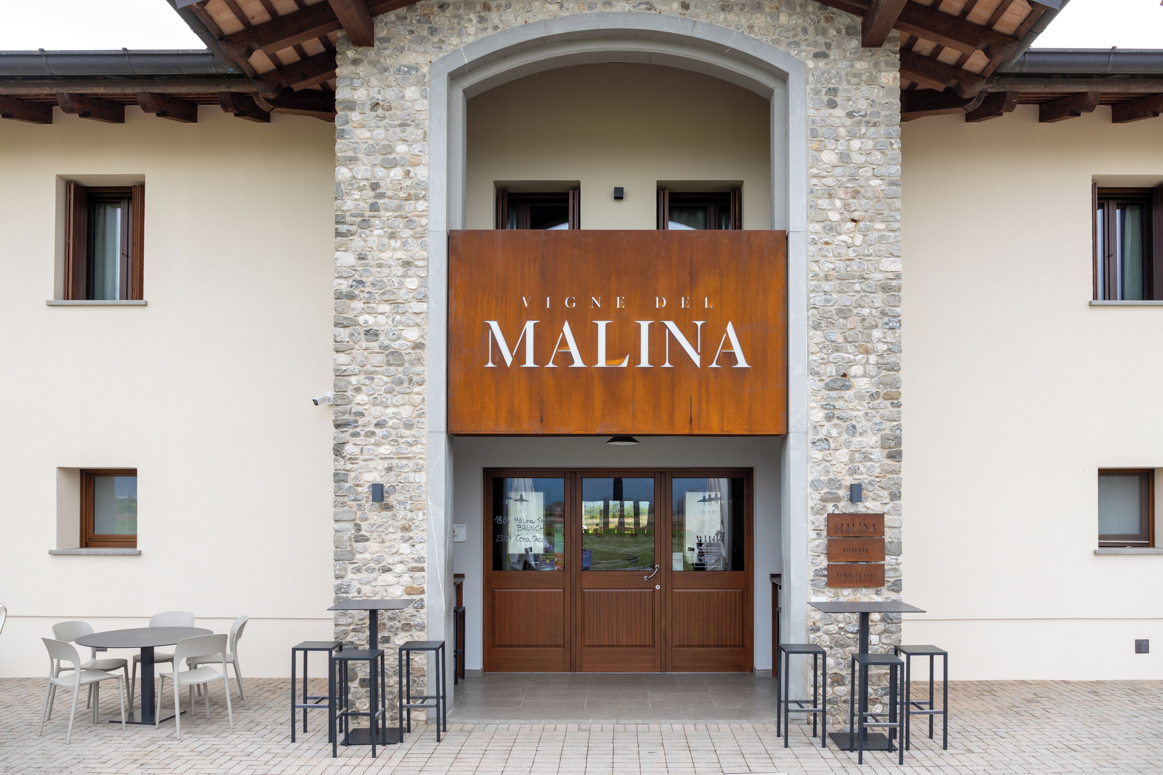 A building with a stone facade and a sign that reads 'VINE DEL MALINA'.