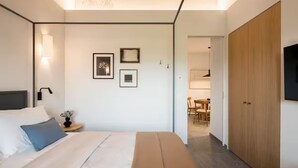 A modern bedroom with a bed, bedside table, wall-mounted light, and a flat-screen TV.