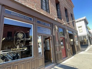 Un edificio de ladrillo con fachada comercial que muestra los rótulos 'ESPRESSO BAR' y 'COMMUNAL CAFE', y un cartel que indica 'ABIERTO 7-18 LUN-SAB'.