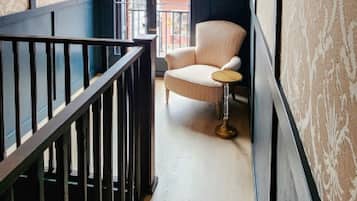 A hallway with a chair and a small table, a railing, and patterned wallpaper.