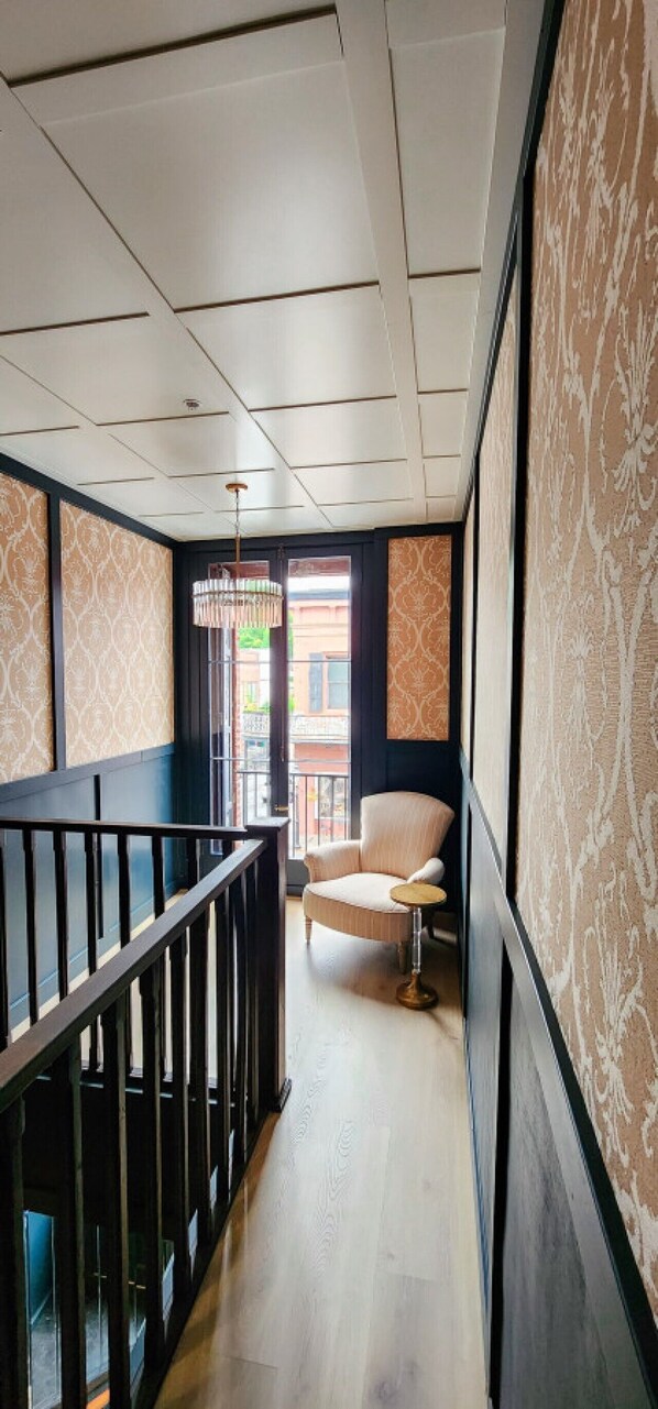 A hallway with a chair and a small table, a railing, and patterned wallpaper.