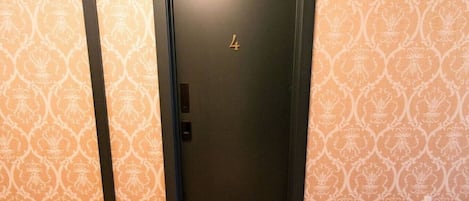 Una puerta con el número 4, ubicada en un pasillo con papel tapiz estampado.