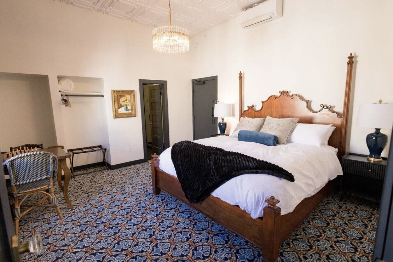 A hotel room with a large bed, a chair, a desk, and a patterned floor.