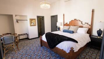 A hotel room with a large bed, a chair, a desk, and a patterned floor.