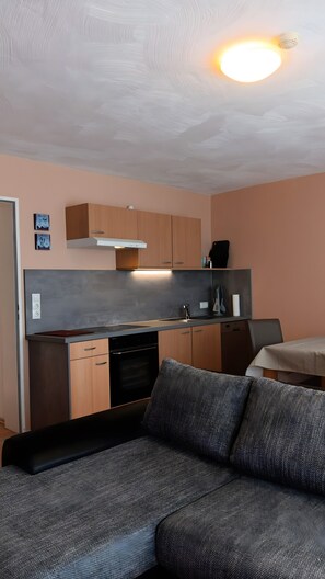 A compact kitchenette with a built-in oven and microwave, a sofa with a textured fabric, and a ceiling light fixture. - Apartment 'Haus Abendsonne Top Floor' with Terrace, Garden & Wi-Fi (Koblenz)