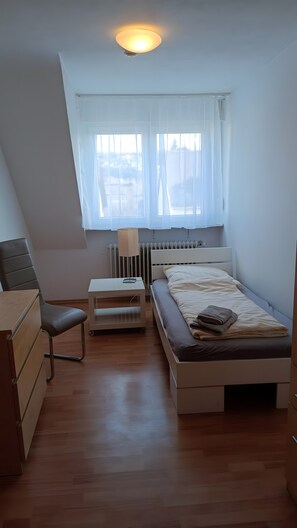 Ein Schlafzimmer mit Bett, Sessel, Schreibtisch und Heizkörper.