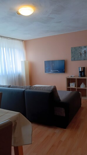 Ein Wohnzimmer mit einer Couch, einer Kaffeemaschine und einem Fernseher an der Wand.