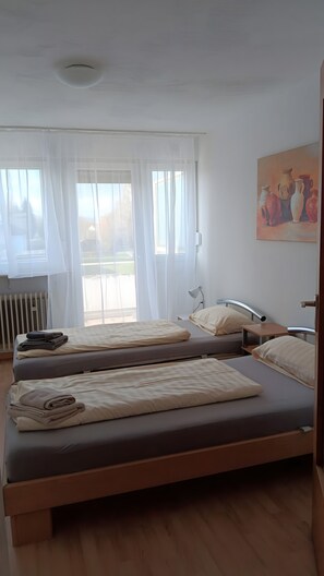A room with two beds, a radiator, a window with sheer curtains, and a painting on the wall. - Apartment 'Haus Abendsonne Top Floor' with Terrace, Garden & Wi-Fi (Koblenz)