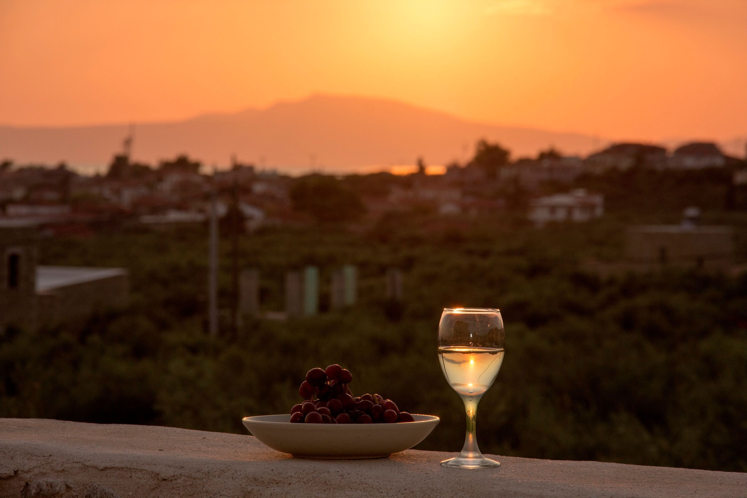 A sunset with a bowl of grapes and a glass of white wine on a ledge.
