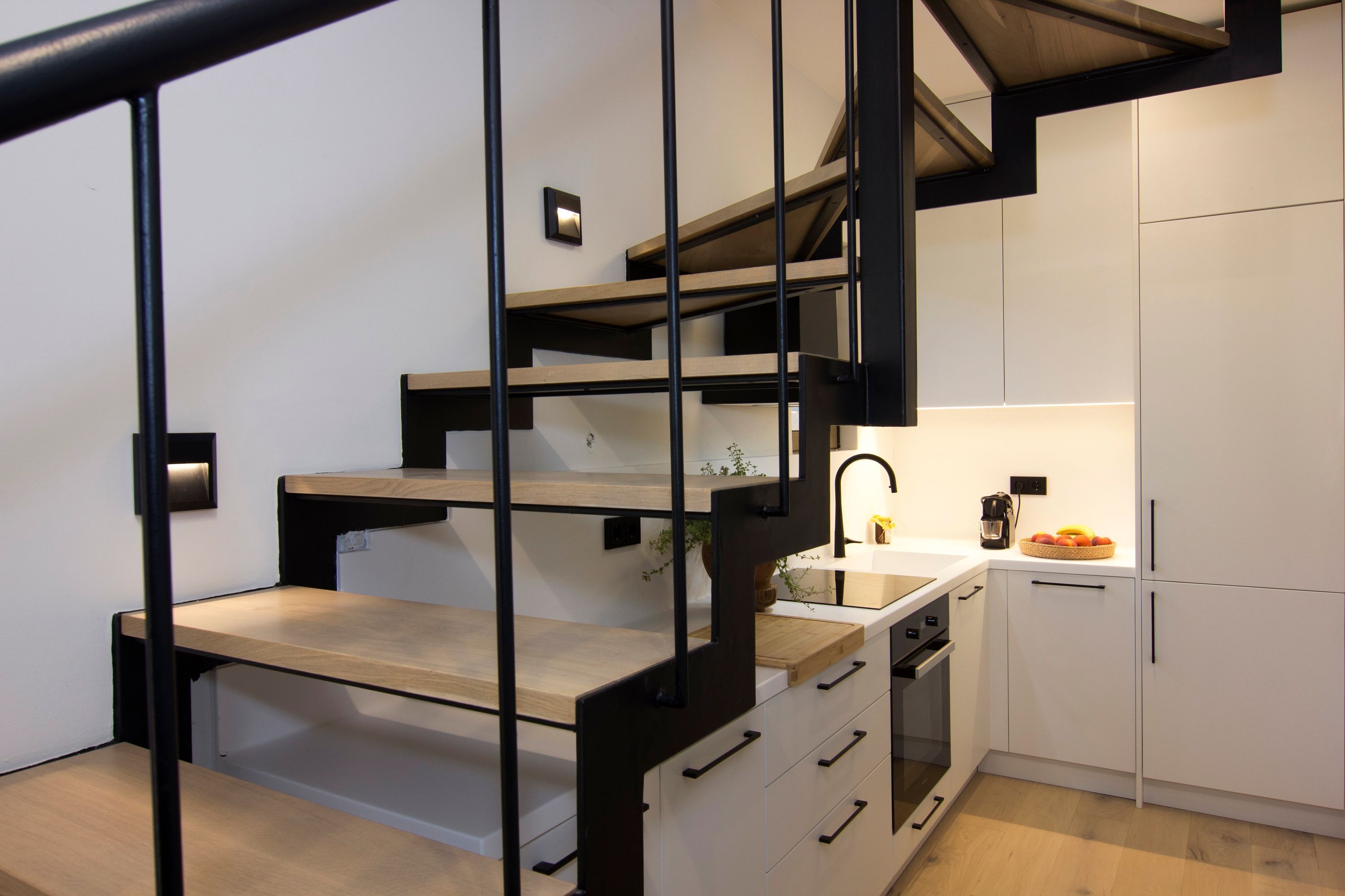 A modern kitchen with a wooden staircase, white cabinets, and a coffee maker on the counter.