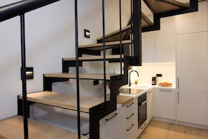 A modern kitchen with a wooden staircase, white cabinets, and a coffee maker on the counter. - Kamak Villa I (West Mani)
