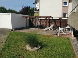 Eine Terrasse mit einer Holzpergola, einem Rasen und einem Fahrradständer.