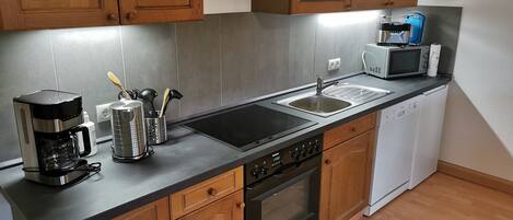 Cocina moderna con armarios de madera, un lavamanos de acero inoxidable, una cafetera, un microondas y un lavavajillas.