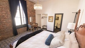 A hotel room with a large bed, a desk, a chandelier, and a view of the bathroom.