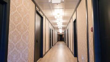 A hotel corridor with patterned wallpaper, wooden flooring, and doors on both sides.