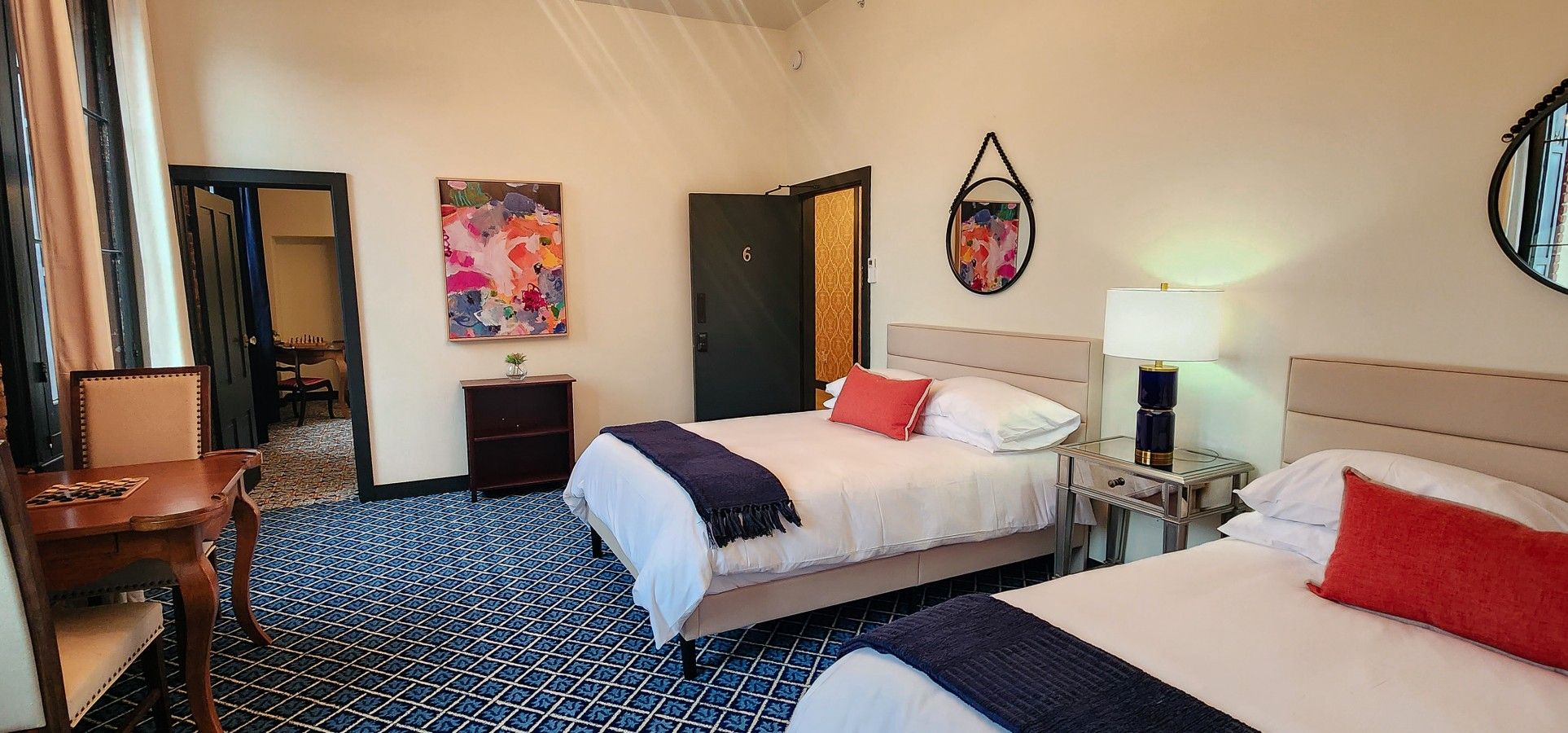 A hotel room with two beds, a desk, a chair, and a small table.