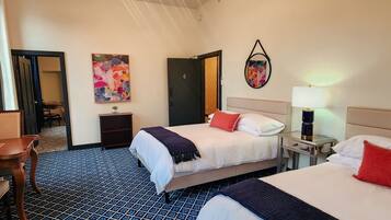 A hotel room with two beds, a desk, a chair, and a small table.