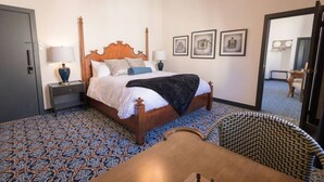 A hotel room with a large bed, two bedside tables, a chandelier, and patterned carpet.