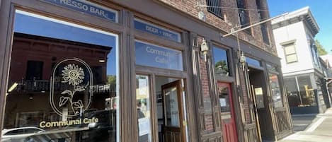 Un edificio con escaparate que indica 'ESPRESSO BAR' y 'CAFETERÍA COMUNITARIA', y un cartel que anuncia 'ABIERTO DE 7 A 18 LUNES A SÁBADO'.
