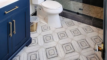 A modern bathroom with a glass shower enclosure, a white toilet, a blue vanity with gold handles, and a large mirror.