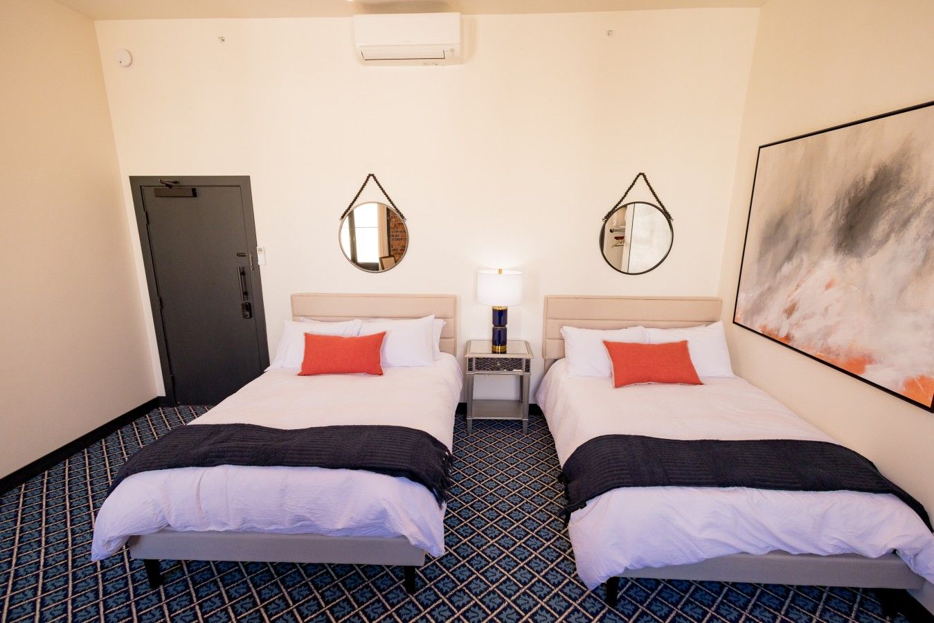 A hotel room with two beds, a nightstand, a mirror, and a painting on the wall.