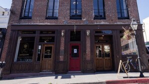 A two-story brick building with a red door, multiple windows, and a small balcony.