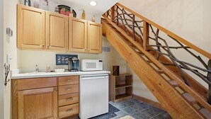 A kitchen with wooden cabinets, a white refrigerator, a microwave, and a coffee maker. There is a wooden staircase with a railing. - Lake, Mountain & Fall Colors-Your Hallmark-Moment (Cullowhee)