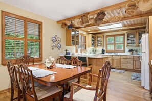 Ein Essbereich mit einem Holztisch und Stühlen, eine Küche mit Holzausstattung und einem Kühlschrank sowie ein Fenster mit Jalousien.