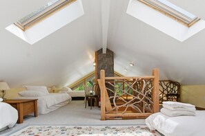 Ein Schlafzimmer mit schrägen Wänden, zwei Dachfenstern, einem Bett, einem Sessel und einer Holzdekoration.