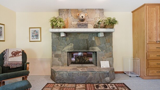 A stone fireplace with a bear decoration, a green armchair, and a wooden cabinet. - Lake, Mountain & Fall Colors-Your Hallmark-Moment (Cullowhee)