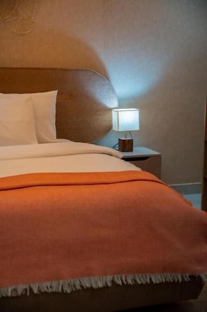 Una cama con cabecera, una mesita de noche con lámpara y una manta.