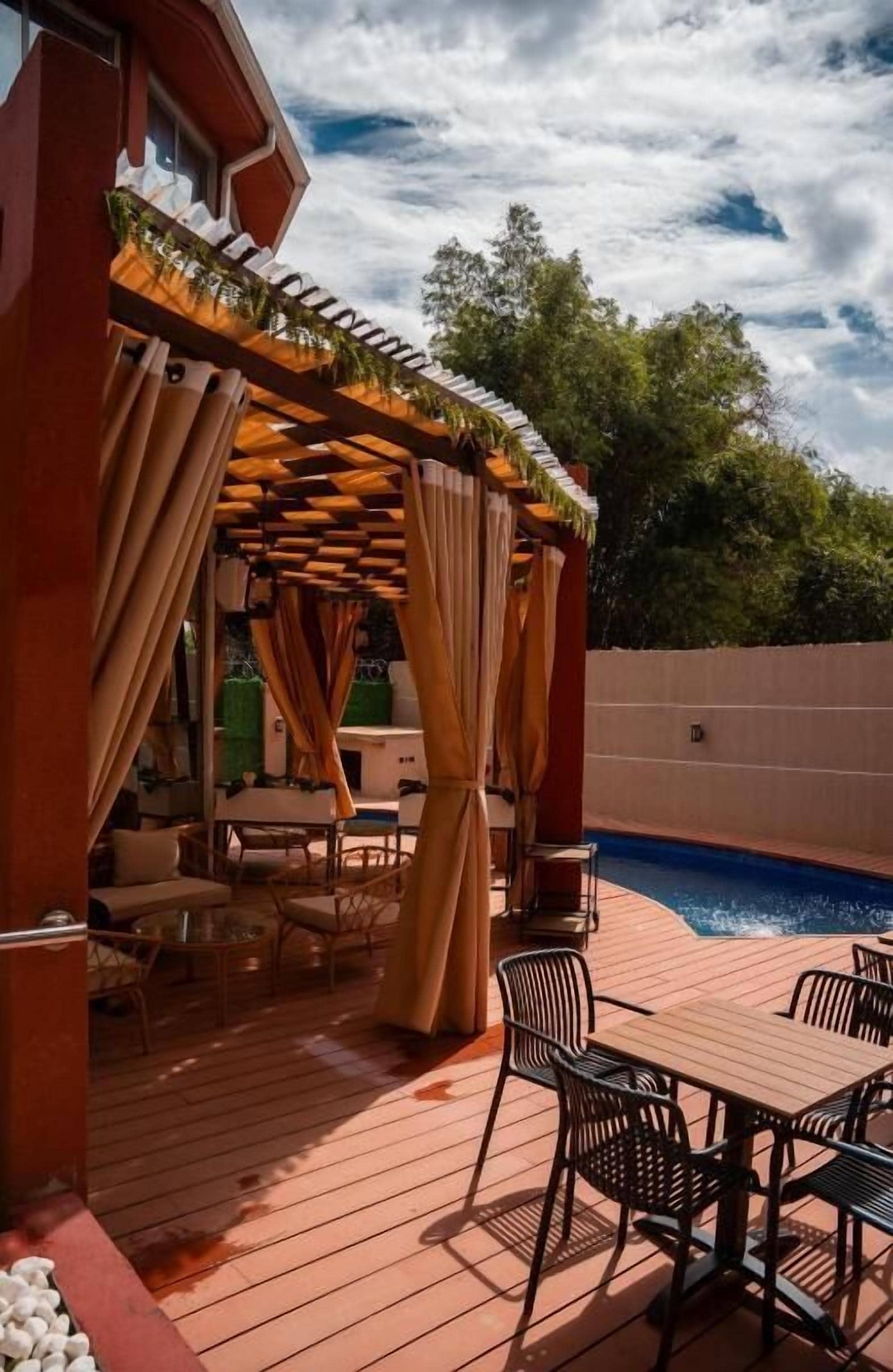 A wooden deck with outdoor furniture, a pool, and a pergola with curtains.