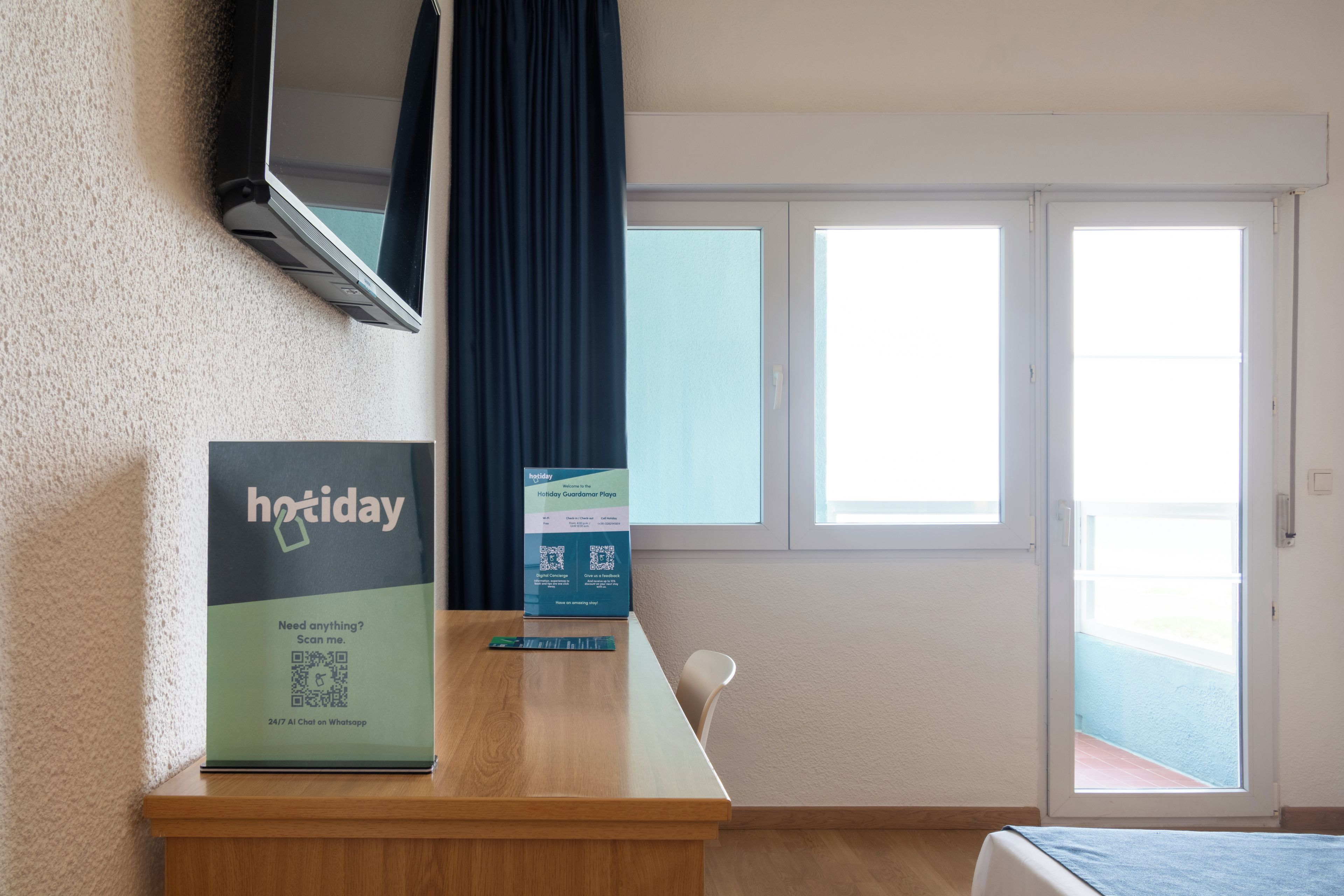 Ein Hotelzimmer mit einem Holztisch, einem flachbildfernseher an der Wand, einem Fenster mit Blick auf den Strand und einem Schild für Holiday Guardian Playa.
