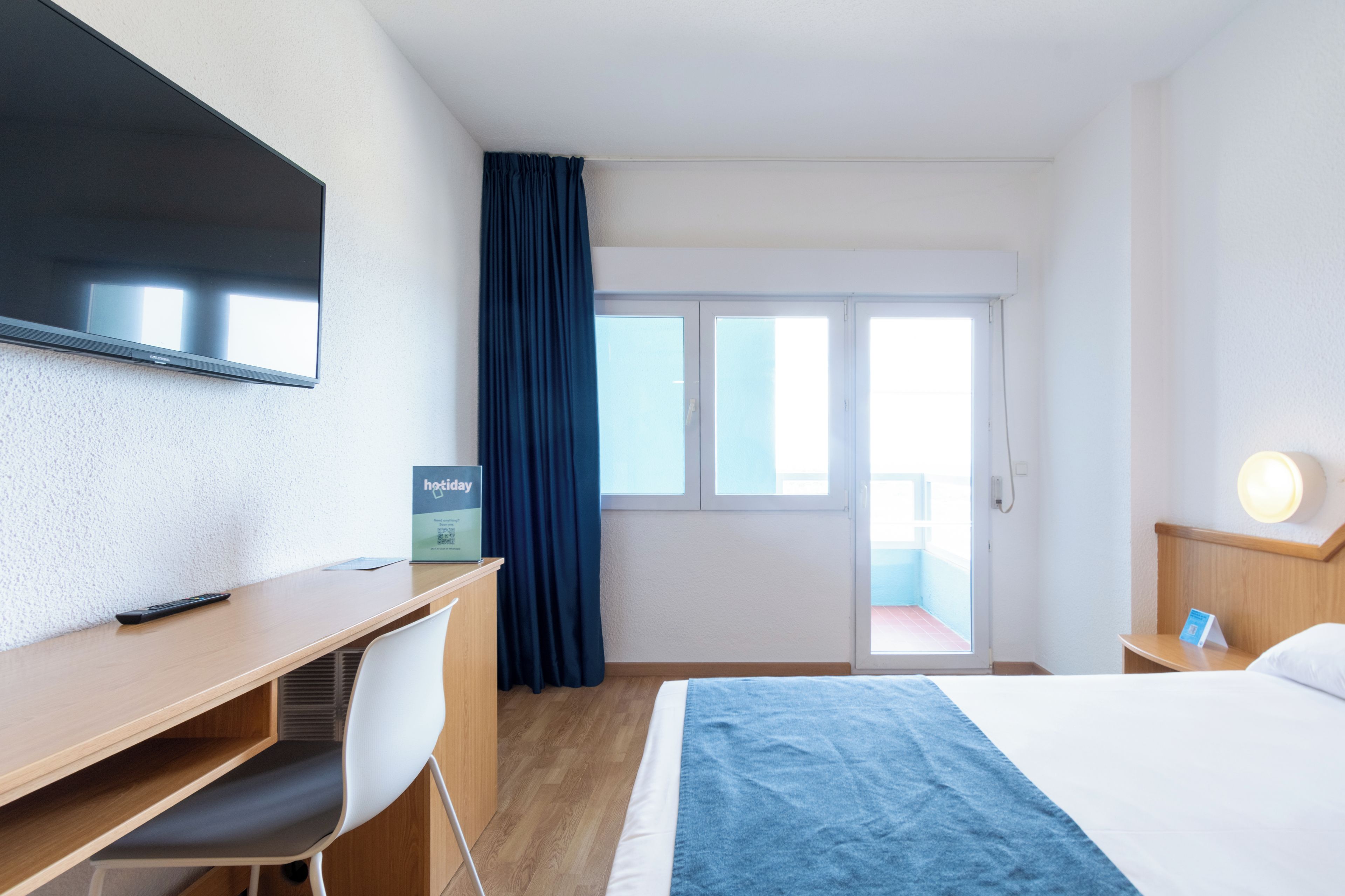 Habitación de hotel con escritorio, silla, cama, televisor y vistas al exterior.