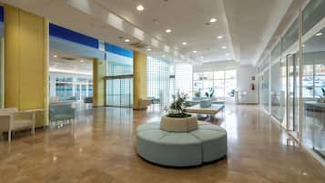 Eine geräumige Lobby mit einer zentralen Sitzecke, Glaswänden und einem modernen Deckenstil.