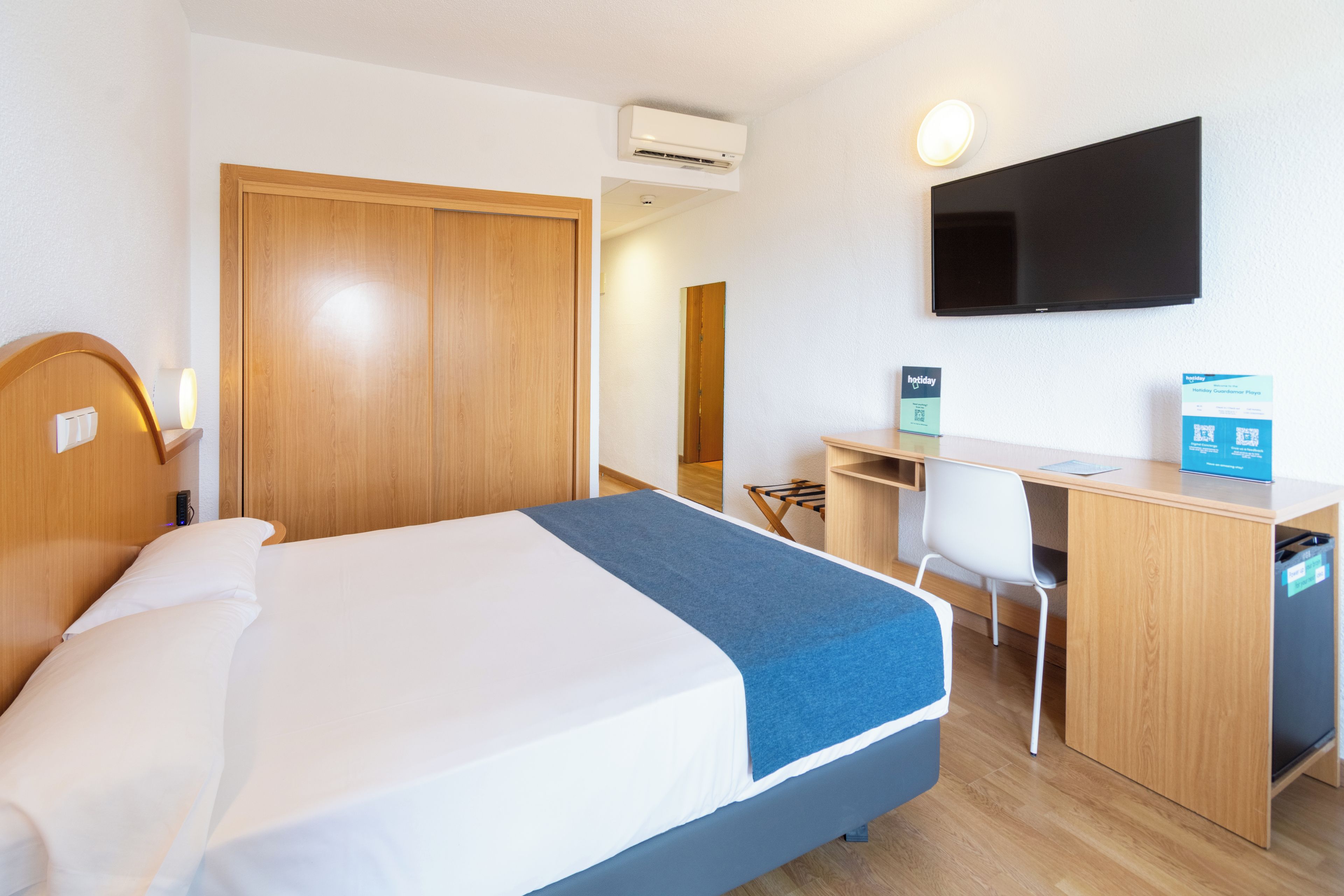 Habitación de hotel con cama, escritorio, silla y televisor de pantalla plana montado en la pared.