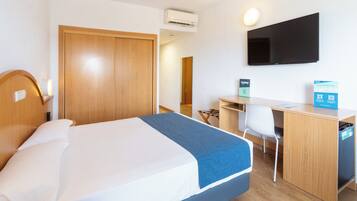 Habitación de hotel con cama, escritorio, silla y televisor de pantalla plana montado en la pared.