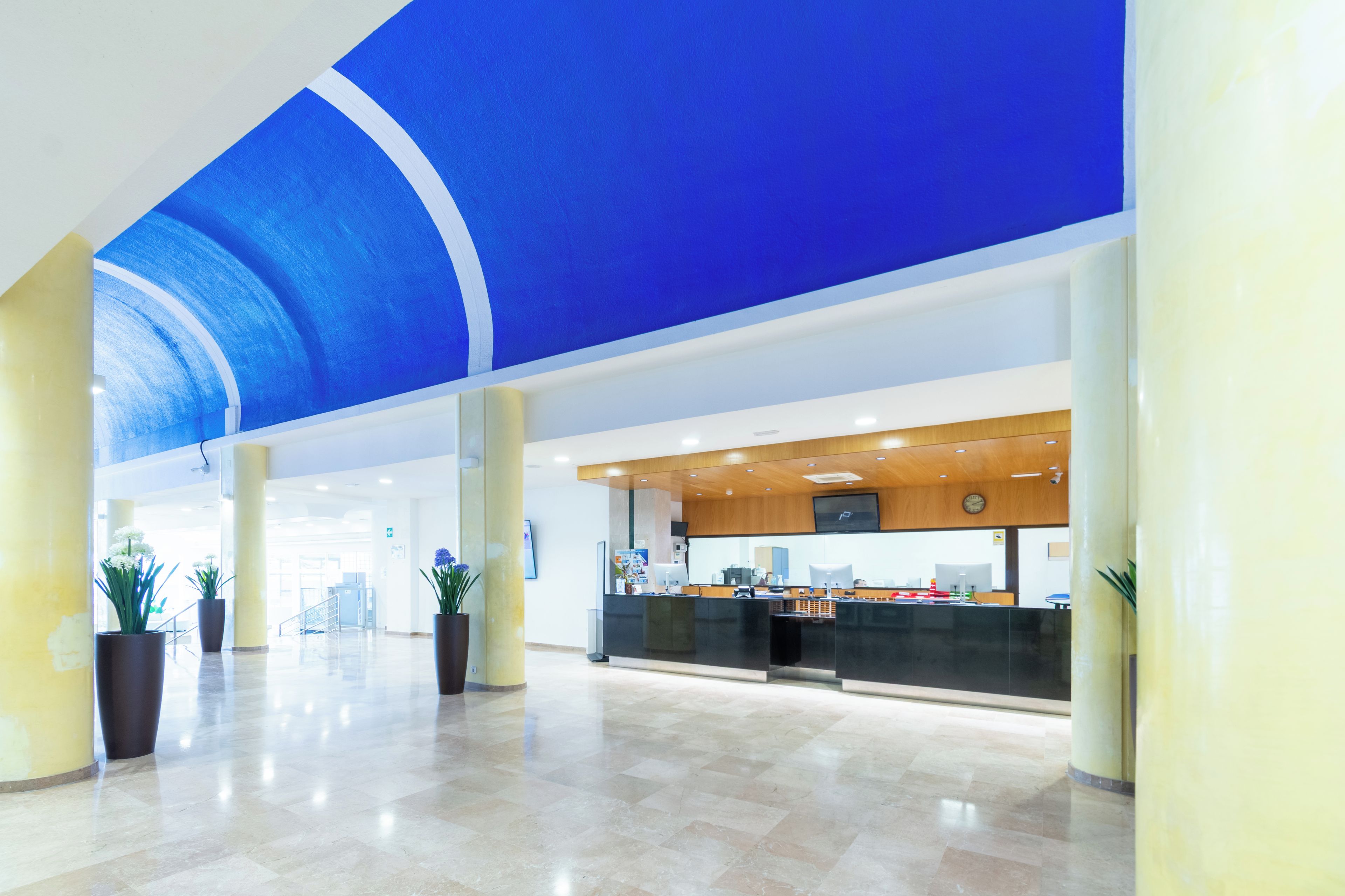 A spacious lobby with a high ceiling, a reception desk, and potted plants.