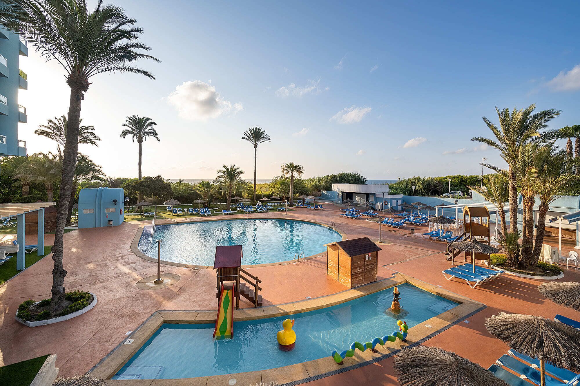 A pool area with a slide, lounge chairs, and palm trees.