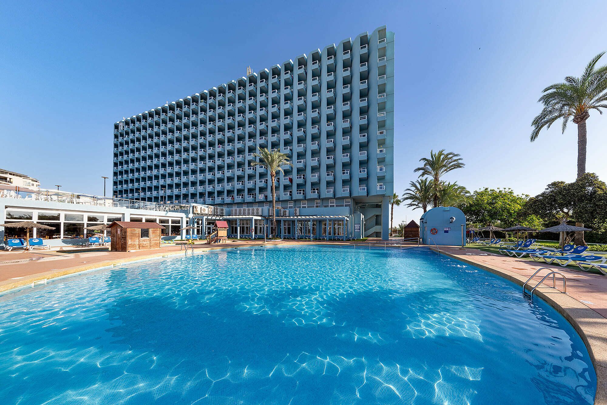 Ett hotell med en stor pool, flera balkonger och palmer.