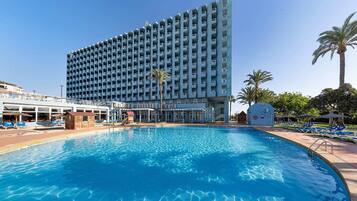 Un hotel con una piscina grande, varios balcones y palmeras.