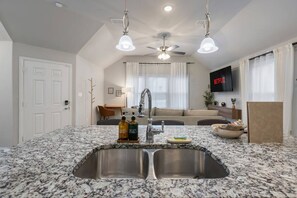 A modern kitchen with granite countertops, stainless steel sink, and overhead lighting.