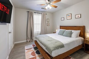 Ein Hotelzimmer mit einem Bett, einem Deckenventilator, einem an der Wand befestigten Fernseher und einem Fenster mit Vorhängen.
