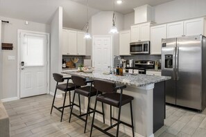 A modern kitchen with a central island, bar stools, stainless steel appliances, and pendant lighting.