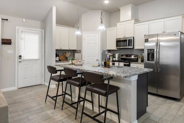 A modern kitchen with a central island, bar stools, stainless steel appliances, and pendant lighting.