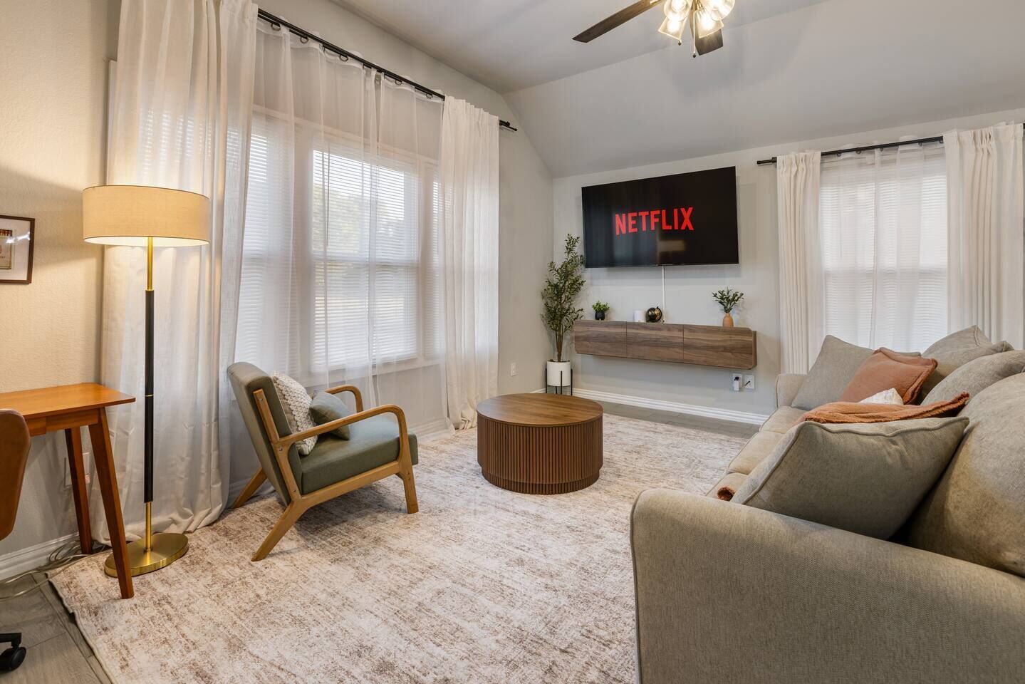 Un salon moderne comprenant un canapé, un fauteuil, une table basse et un téléviseur à écran plat fixé au mur.